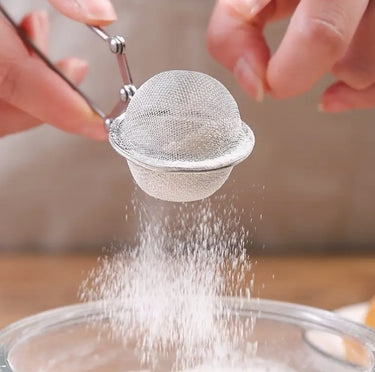 Metal mesh strainer being used to sprinkle a powdery substance over a dish.